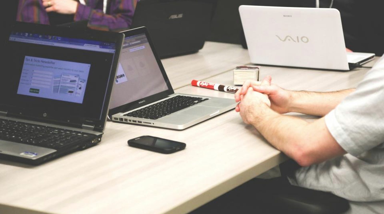 A shared work table with several open laptops of different brands and a marker pen - each person bringing their own tools into shared work