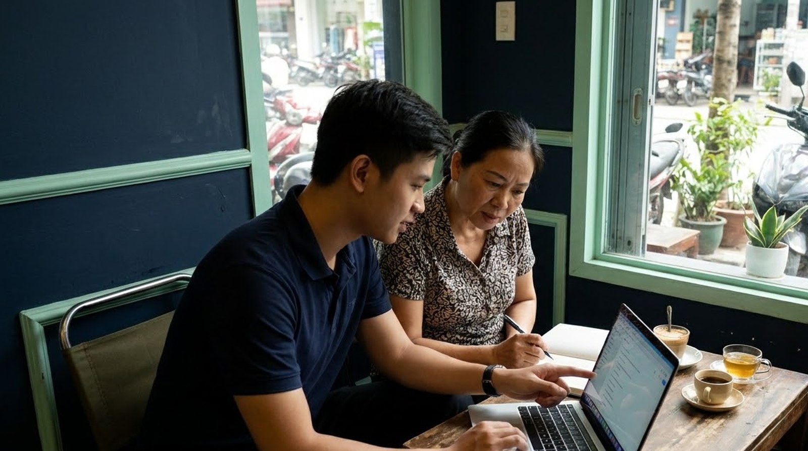 A consultant points at a chatbot quote on a laptop while a shop owner takes notes at a cafe table