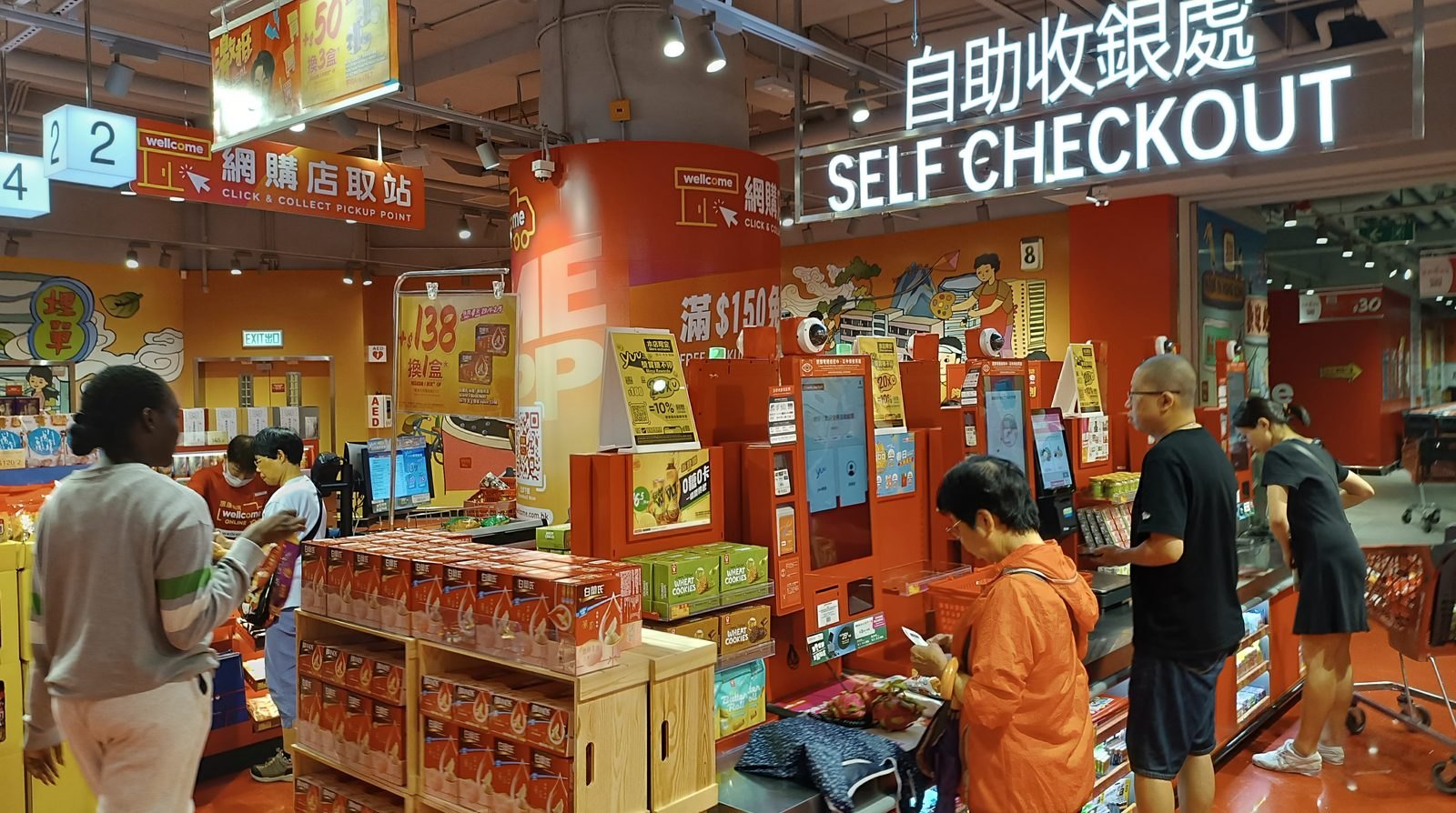 Shoppers at a self checkout counter in an Asian supermarket surrounded by promotional signage and a click and collect pickup point