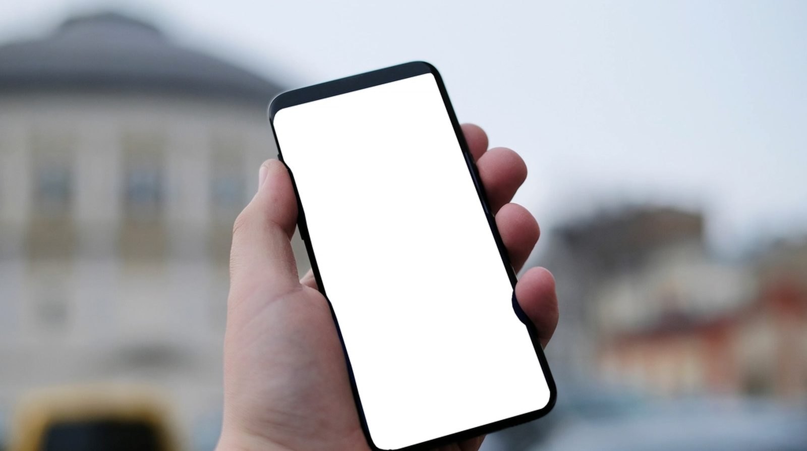 A hand holding a smartphone with a blank screen against a street backdrop, illustrating an ad appearing on a customer's phone