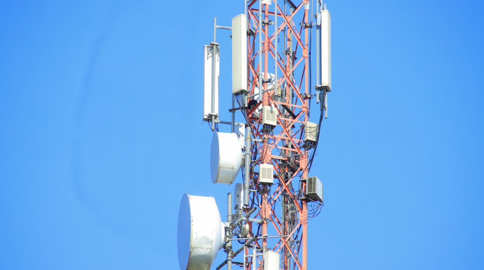 A telecommunications mast carrying antennas and microwave dishes against a blue sky, illustrating the group of systems operating critical technical infrastructure covered by the high-risk AI list