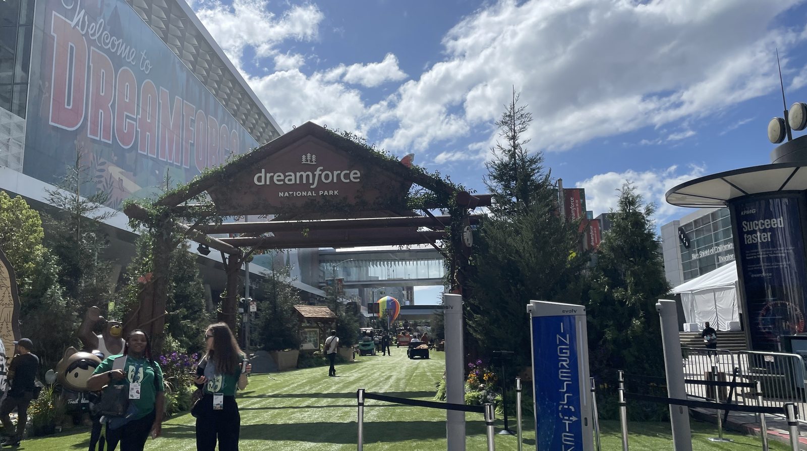 The entrance to the Dreamforce event area with a wooden dreamforce national park sign and badge-wearing attendees on artificial grass in front of the conference building